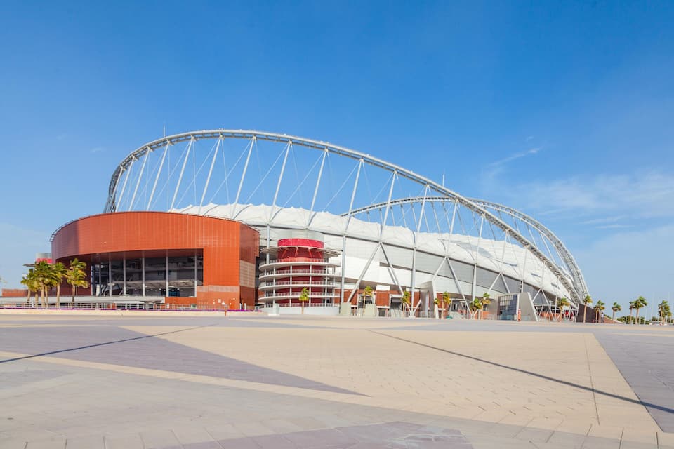 A modern stadium with a large arch and a red building adjacent to it.