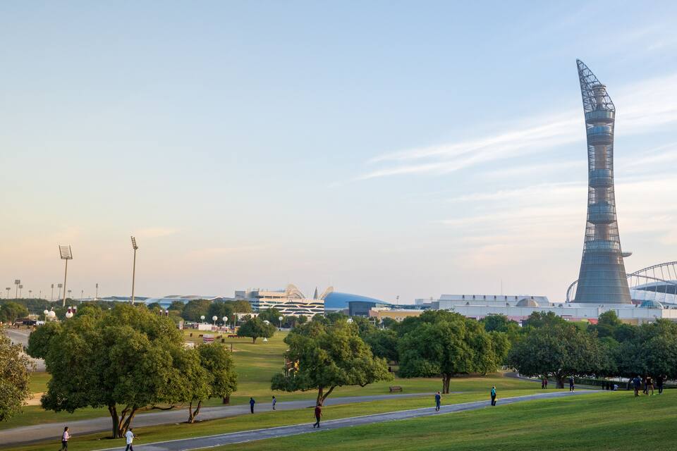 A cityscape with a prominent tower, a stadium, and a park with trees and a pathway.