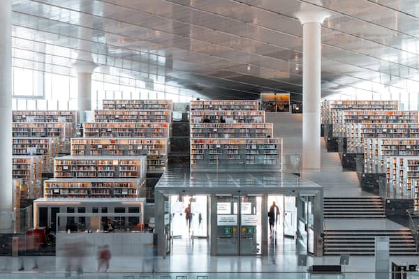 Eine moderne Bibliothek mit mehreren Etagen voller Bücherregale und einer zentralen Treppe.