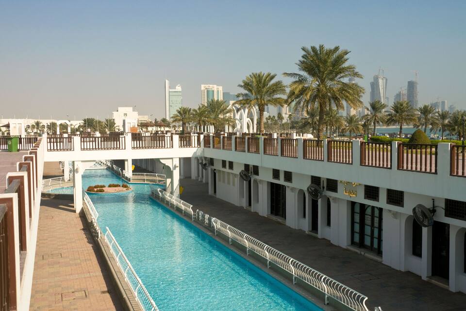 Una piscina con un puente, palmeras y edificios modernos al fondo.