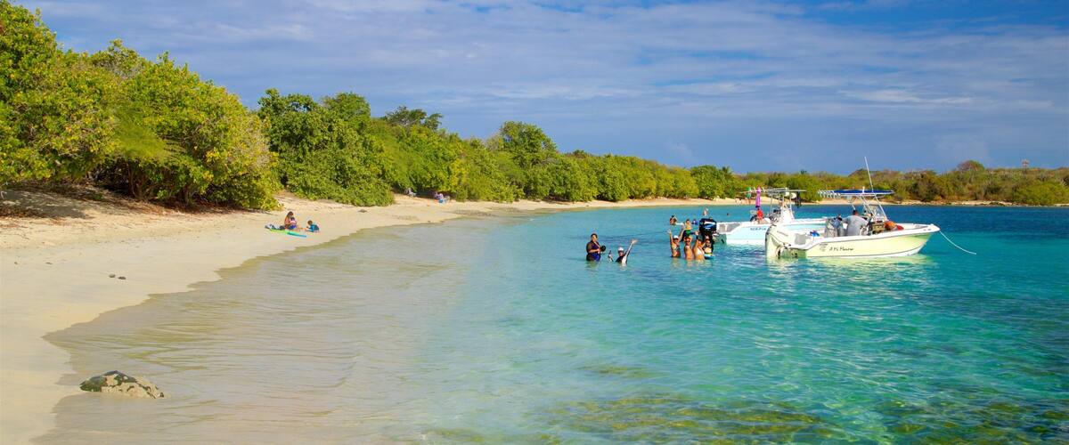 A beach with clear turquoise water, a boat anchored near the shore, and lush green vegetation along the coastline.