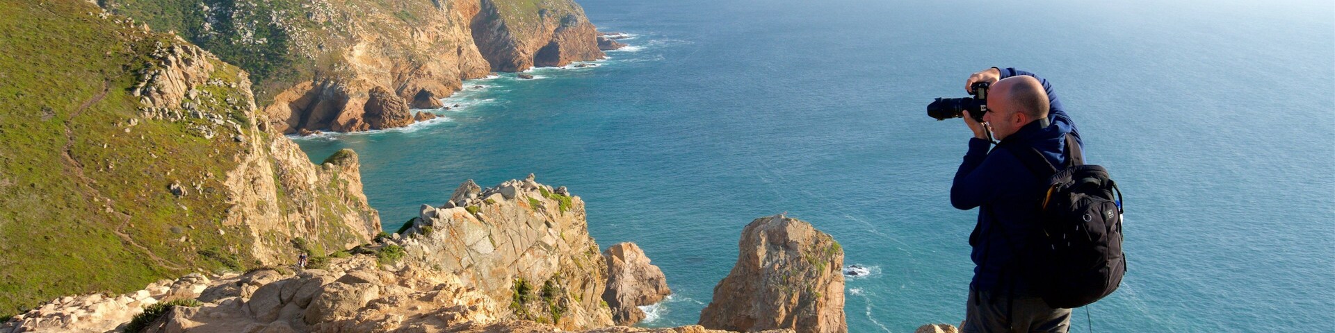 Une personne prend une photo d'un paysage côtier, avec des falaises rocheuses et l'océan.