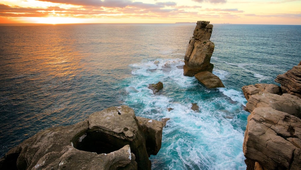 A coastal rock formation with a hole, ocean waves, and a sunset.