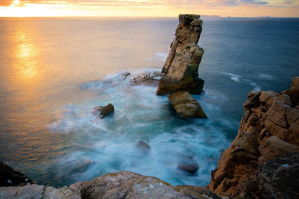Une formation rocheuse côtière au coucher du soleil, avec des vagues qui s'y brisent.