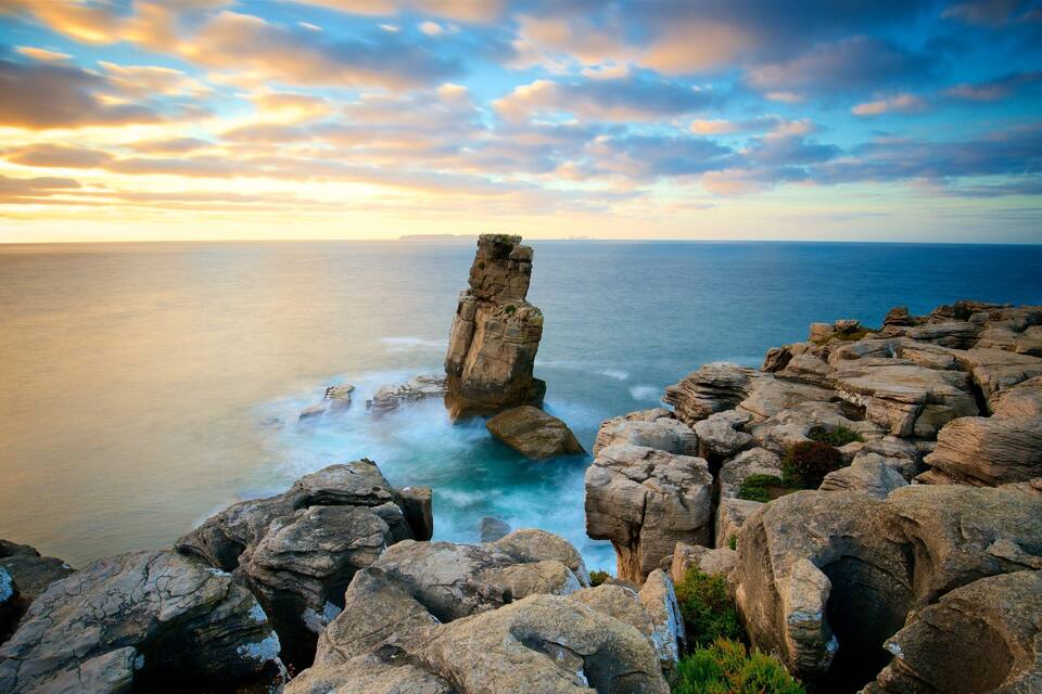 A coastal rock formation with a prominent pillar-like structure surrounded by rugged terrain and the ocean.