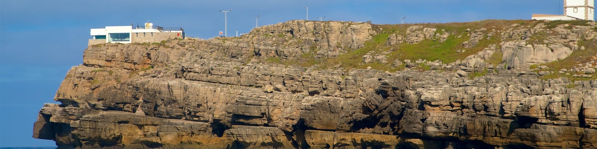 A rocky cliff with a lighthouse and a modern building on top.