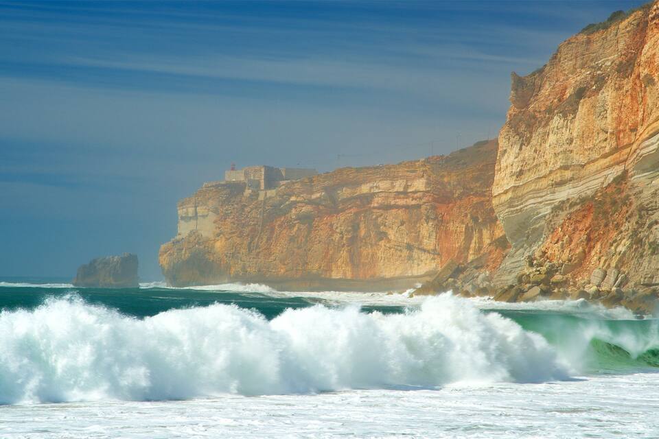 A coastal cliff with layered rock formations and a lighthouse.