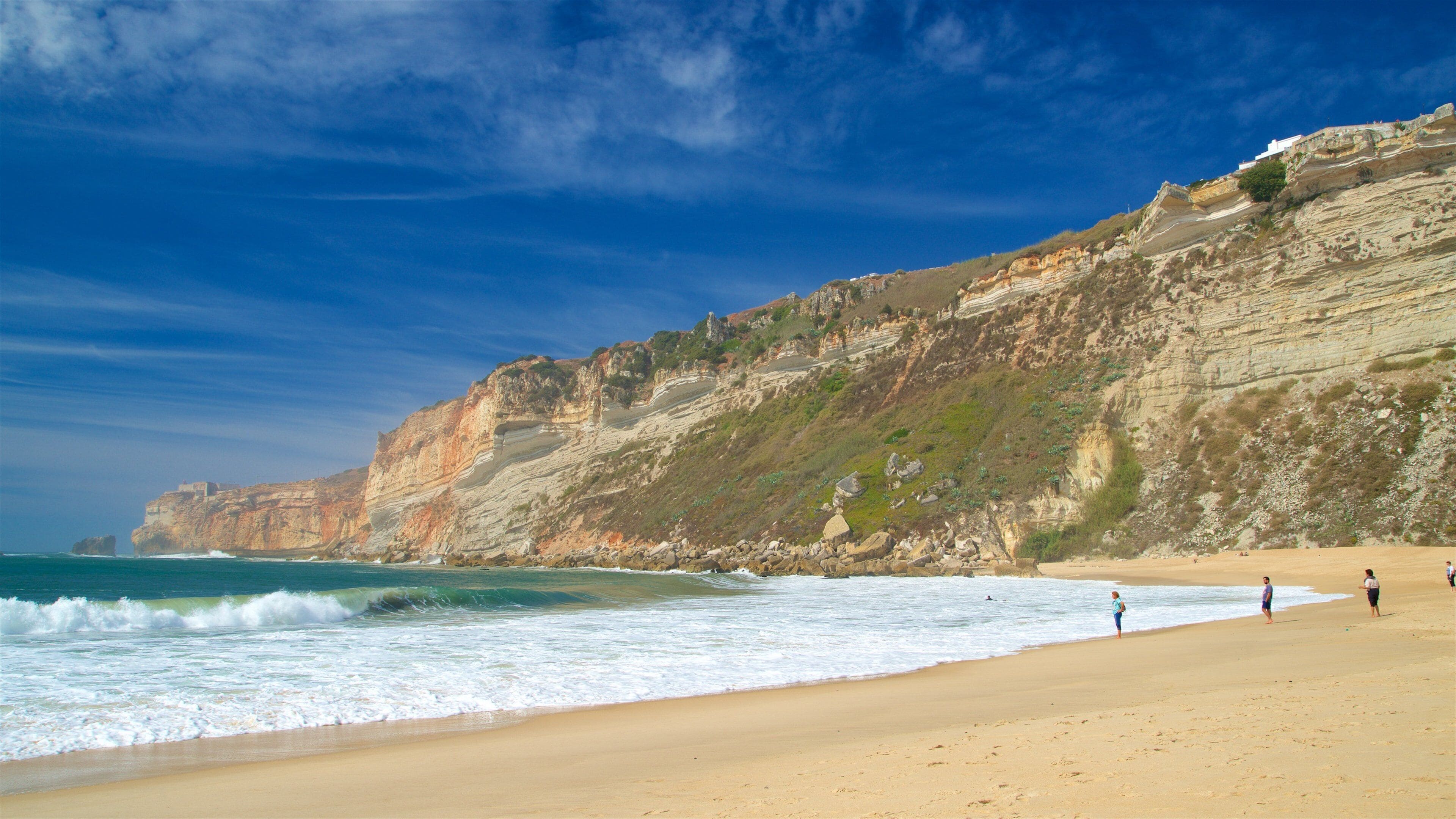 Eine Küstenlandschaft mit Sandstrand, felsigen Klippen und blauem Himmel.