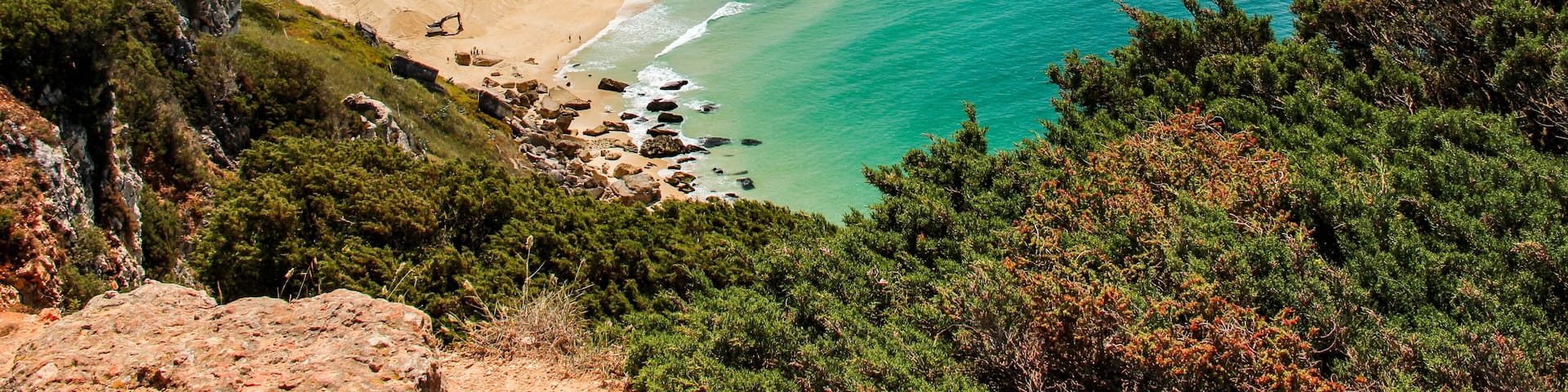 A coastal town with a sandy beach, turquoise waters, and red-roofed buildings.