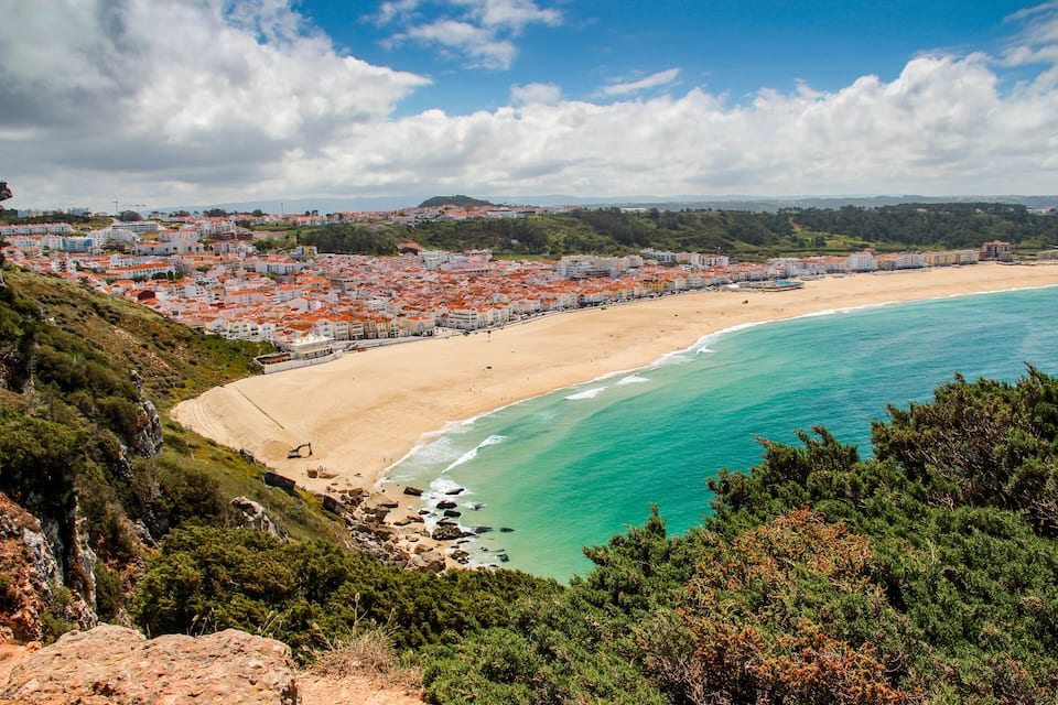 Une ville côtière dotée d’une plage de sable, d’eaux turquoise et de bâtiments aux toits rouges.