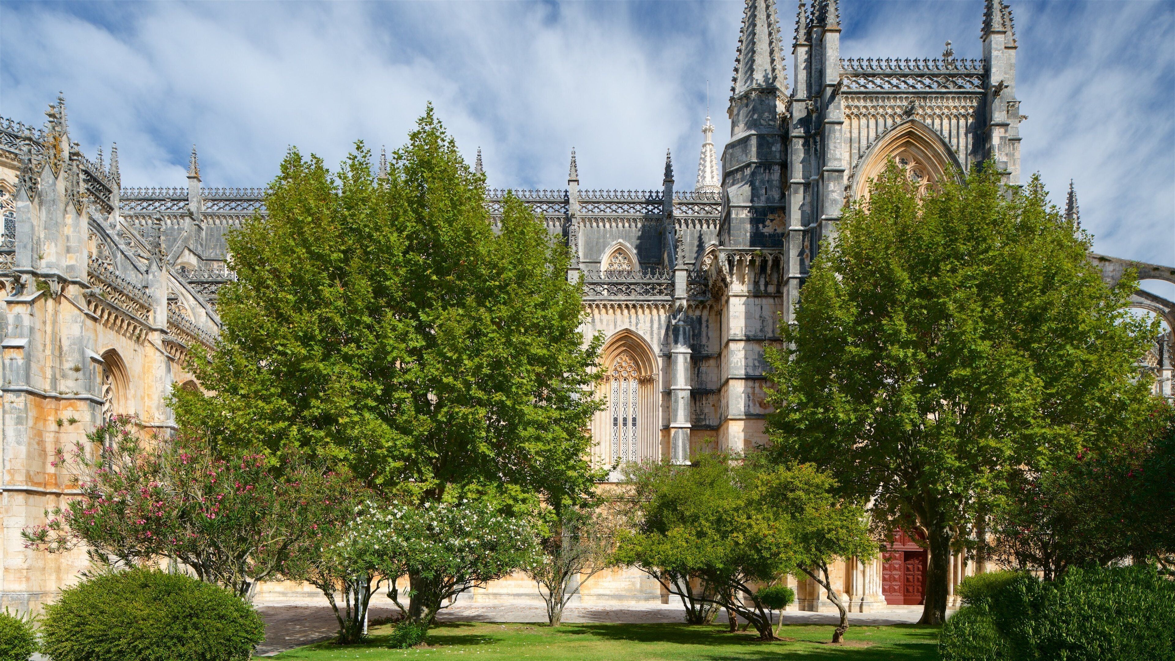 Una catedral histórica con intrincada arquitectura gótica, rodeada de exuberantes árboles verdes y un césped cuidado.