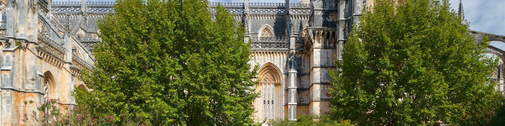Una catedral histórica con intrincada arquitectura gótica, rodeada de exuberantes árboles verdes y un césped cuidado.