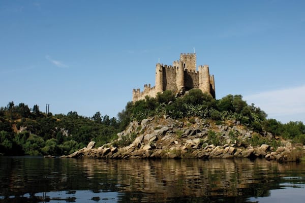 A castle on a rocky hill overlooking a calm body of water.