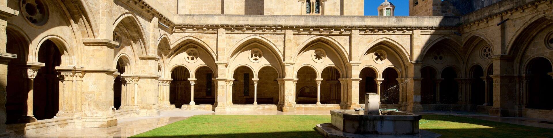 A historic courtyard with a fountain, surrounded by arched walkways and a prominent castle-like building with a tower.
