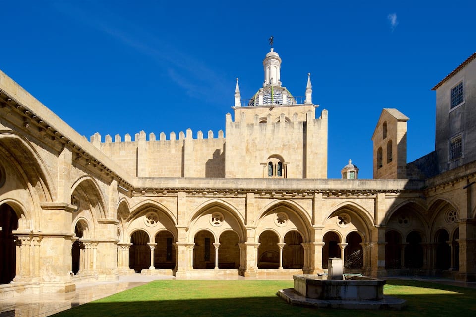 A historic courtyard with a fountain, surrounded by arched walkways and a prominent castle-like building with a tower.