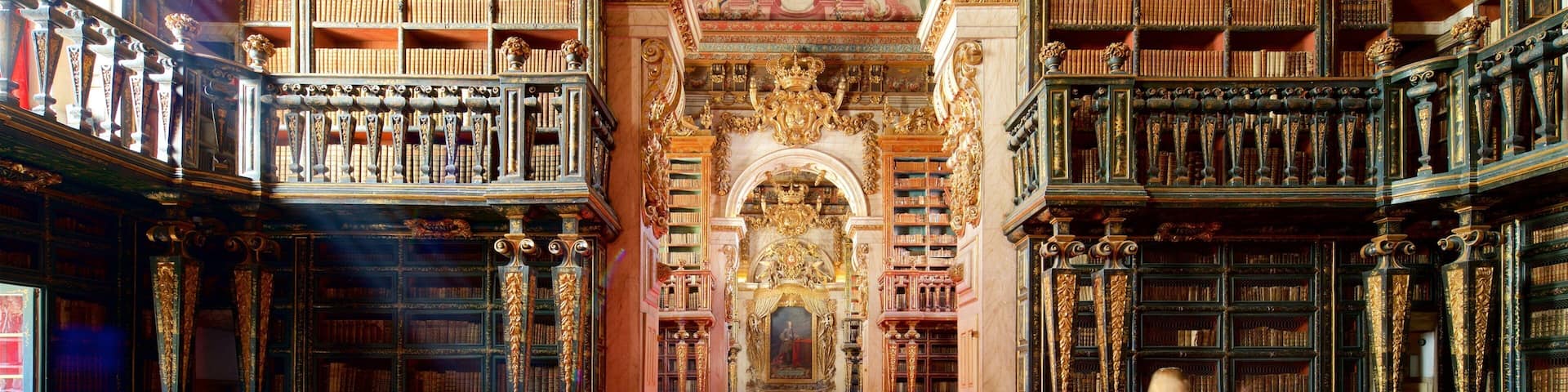 A grand library with ornate bookshelves, a red carpet, and a central ornate archway.
