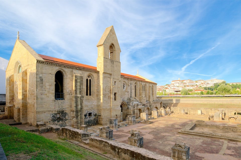 Une église de pierre ancienne, avec un toit recouvert de tuiles rouges et un clocher, entourée de ruines et avec une rivière en arrière-plan.