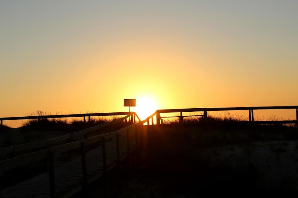 A wooden boardwalk leading to a beach at sunset.