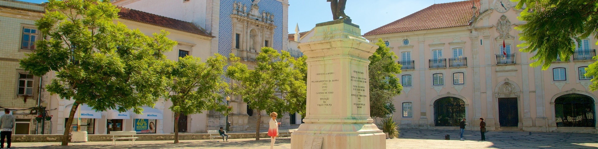 Uma praça com uma estátua, edifícios históricos e calçada de pedra.
