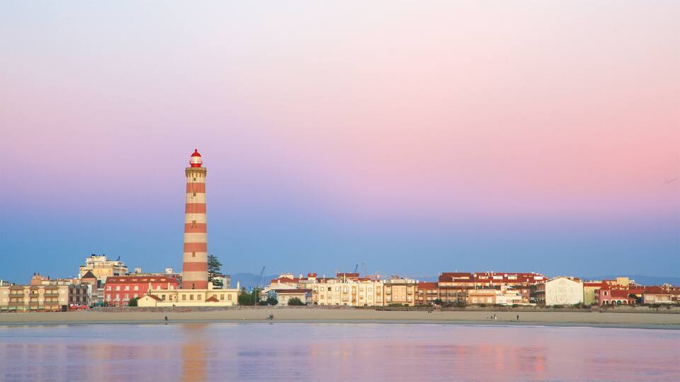 A coastal town with a prominent red and white striped lighthouse, a sandy beach, and a row of colorful buildings.