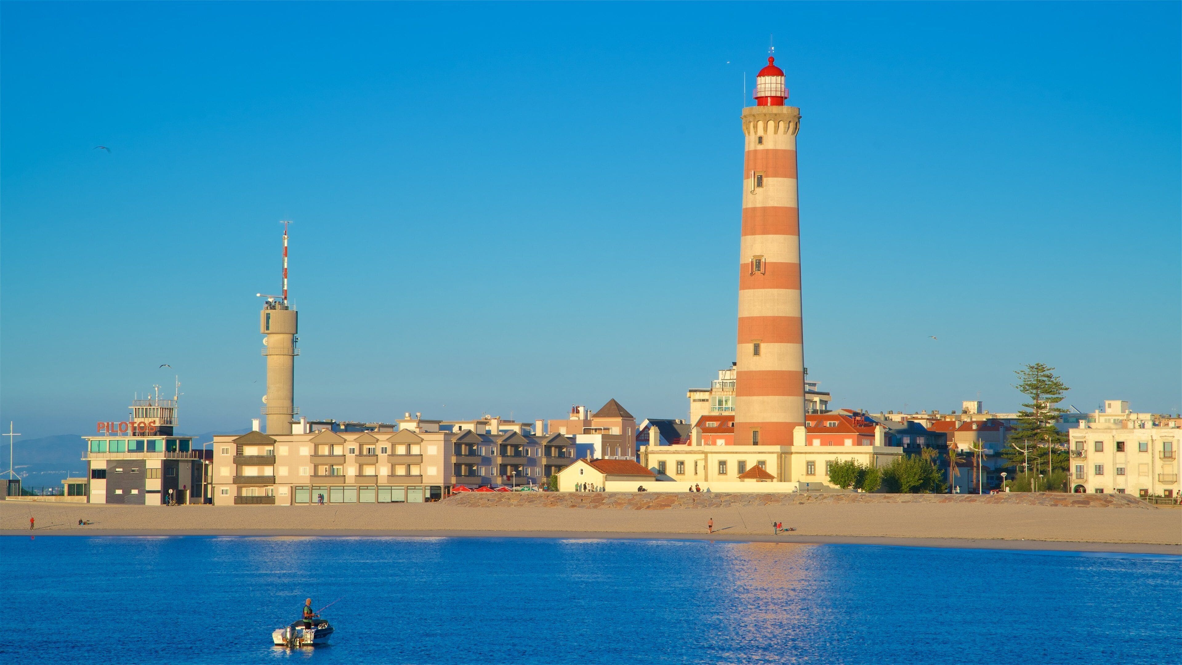 A coastal town with a prominent lighthouse, a control tower, and a beach with people fishing.