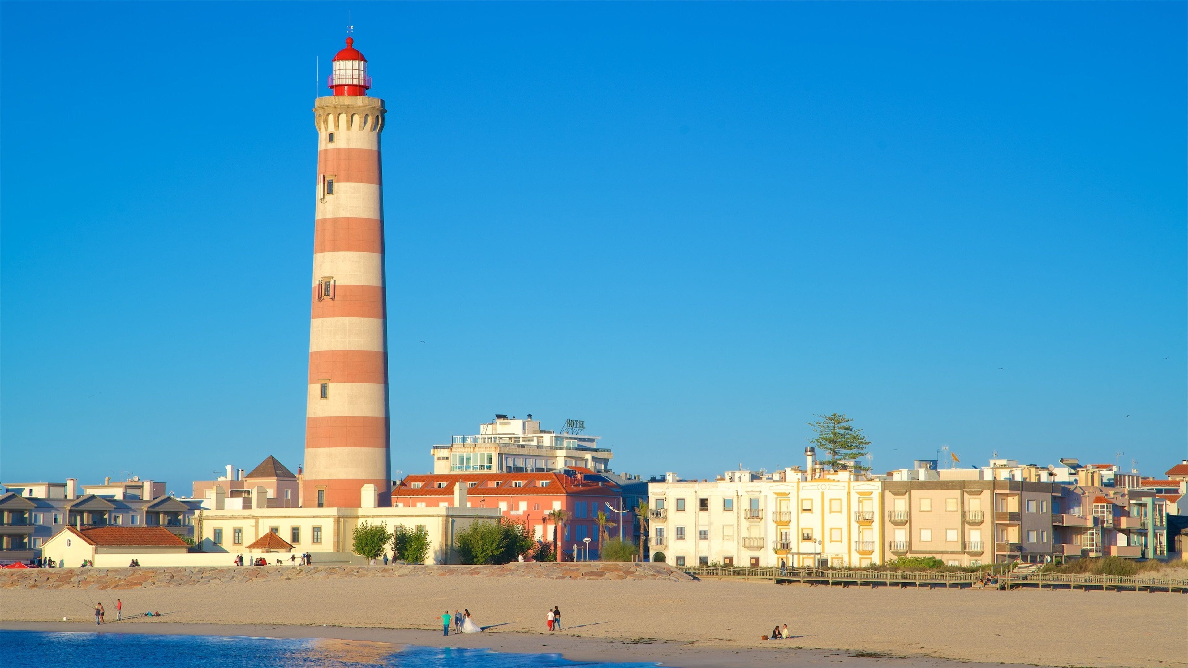 A coastal town with a prominent lighthouse, colorful buildings, and a beach.