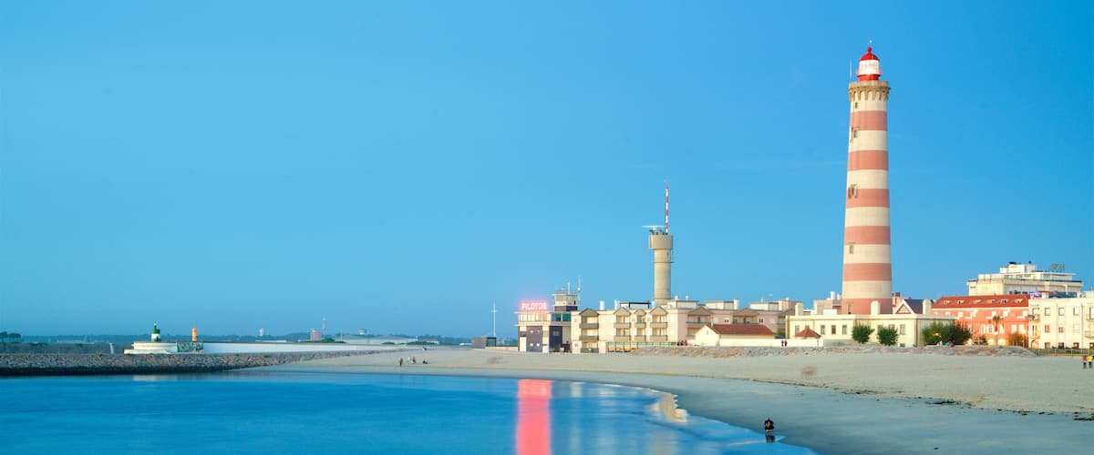 A coastal scene with a lighthouse, beach, and buildings.