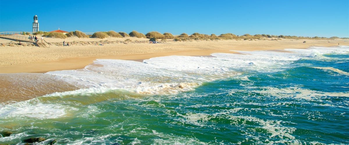 A beach with waves, a lighthouse, and a person paragliding.