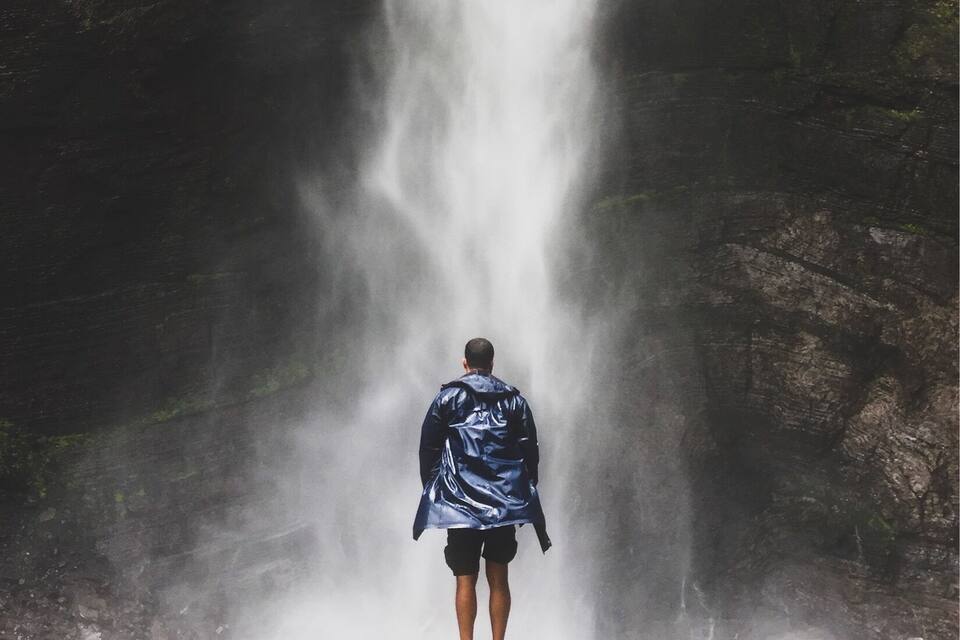Una cascada con una persona de pie en su base.