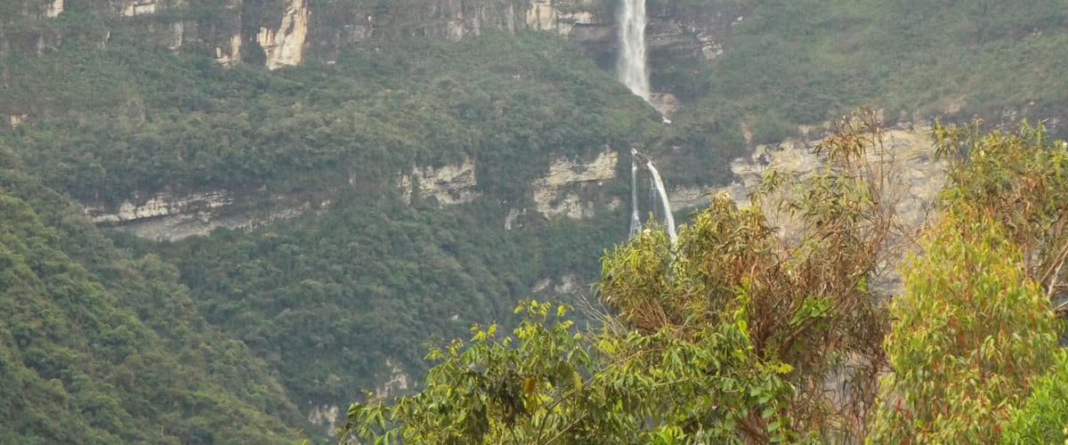 A waterfall cascading down a steep cliff surrounded by dense forest.