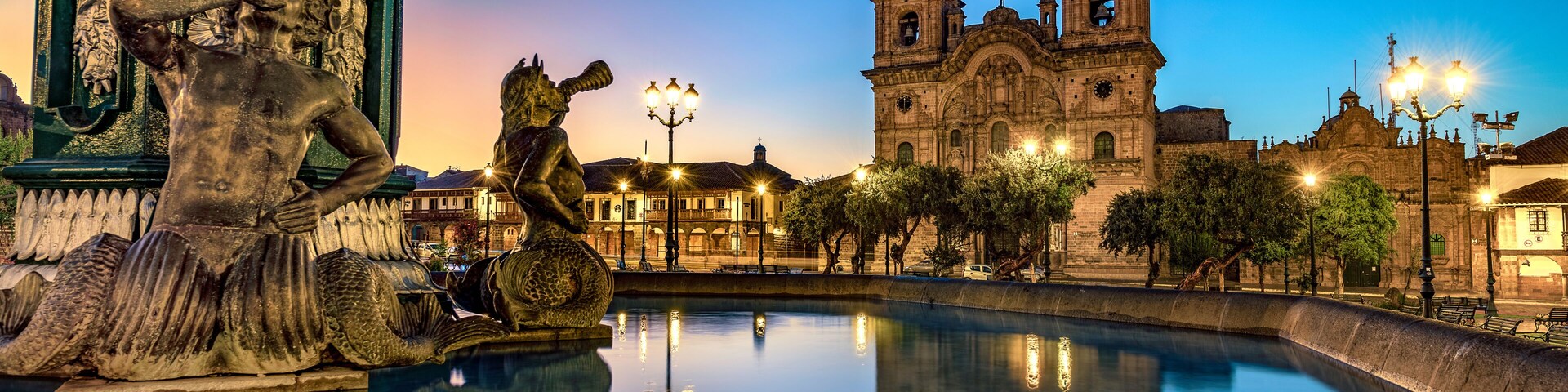 Uma fonte histórica com uma estátua, um espelho d'água e uma catedral ao fundo.