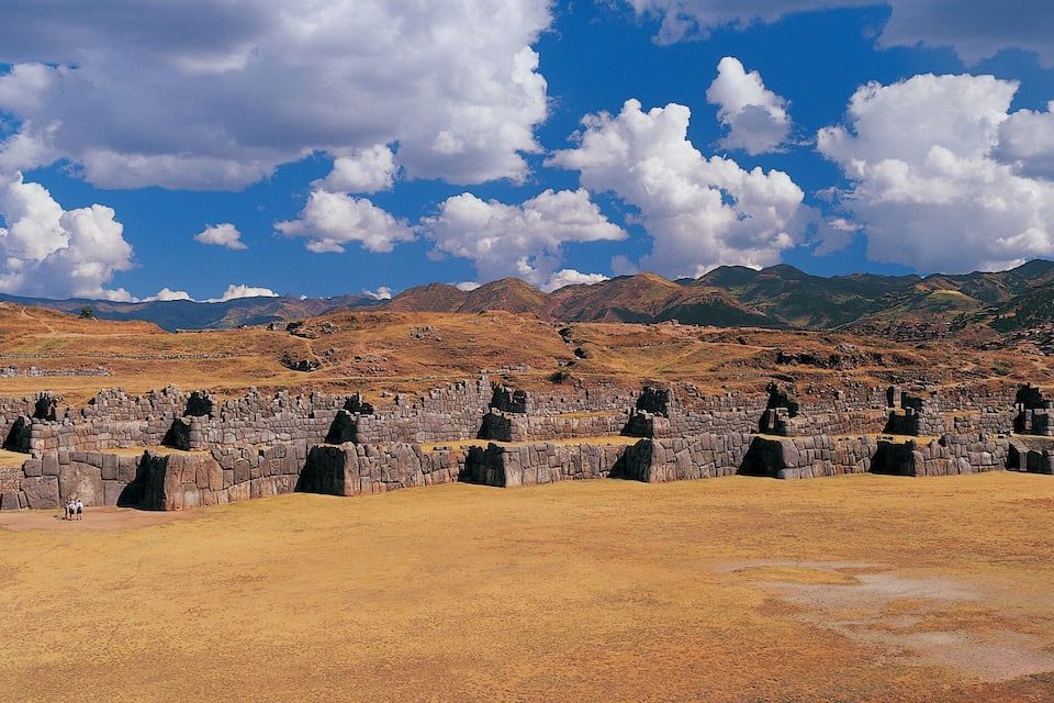 Ancient stone ruins in a dry, hilly landscape with a clear sky.