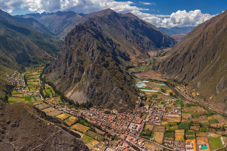 A mountainous landscape with a town nestled in a valley, surrounded by terraced fields and steep cliffs.