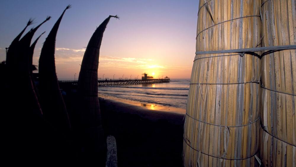 A row of traditional reed fishing boats against a sunset on the main beach front and pier of Punta Sal in Peru
