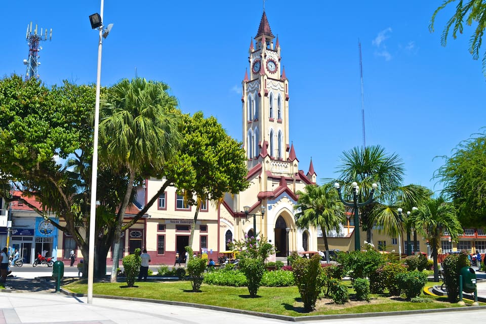 A historic building with a clock tower, surrounded by lush greenery and palm trees.