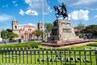 A statue of a mounted figure, a historic building with a bell tower, and a well-maintained garden with geometric hedges.