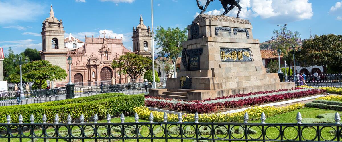 A statue of a mounted figure, a historic building with a bell tower, and a well-maintained garden with geometric hedges.