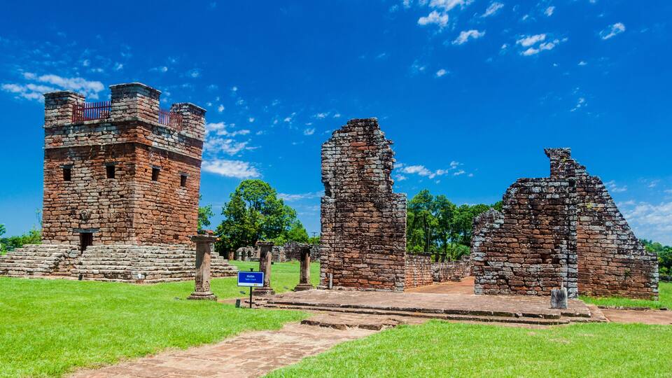 Ancient ruins with a tower, stone pillars, and a clear blue sky.