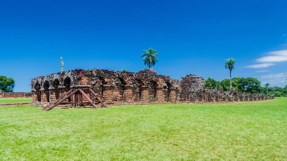 An ancient stone structure with arches and a palm tree in the foreground.