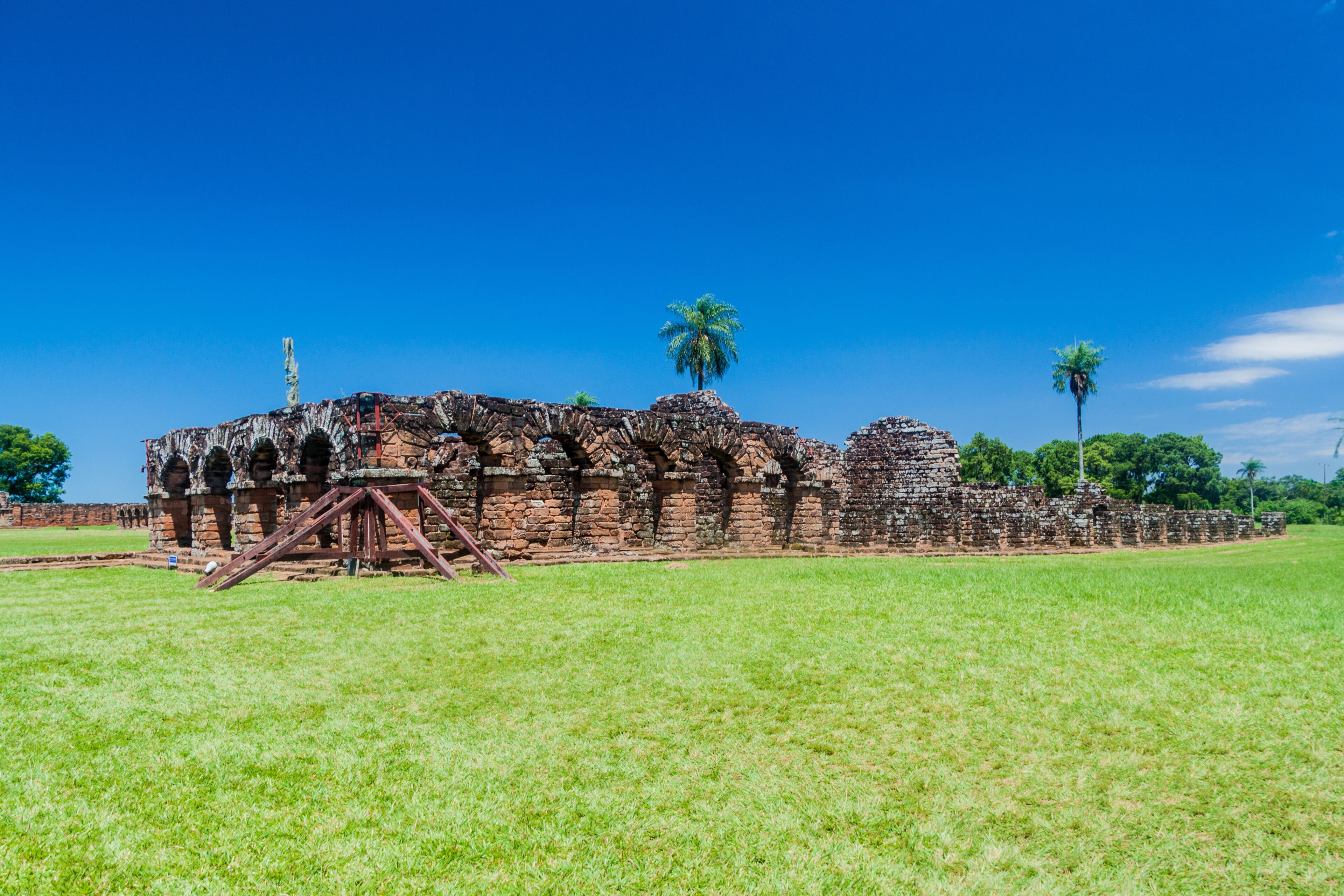 An ancient stone structure with arches and a palm tree in the foreground.