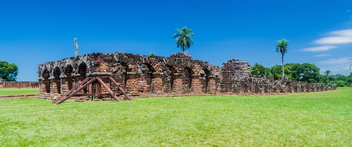 An ancient stone structure with arches and a palm tree in the foreground.