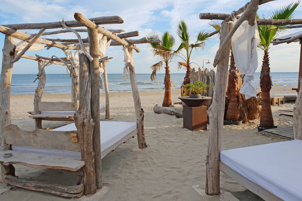 A beach with wooden structures, palm trees, and a sandy shore.