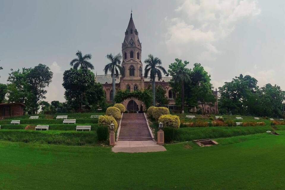 A church with a tall tower and steps leading up to it, surrounded by greenery and palm trees.