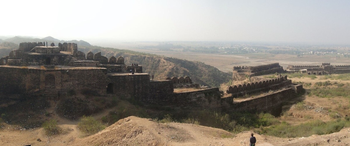 A historical fort with multiple walls and towers, surrounded by hilly terrain and sparse vegetation.
