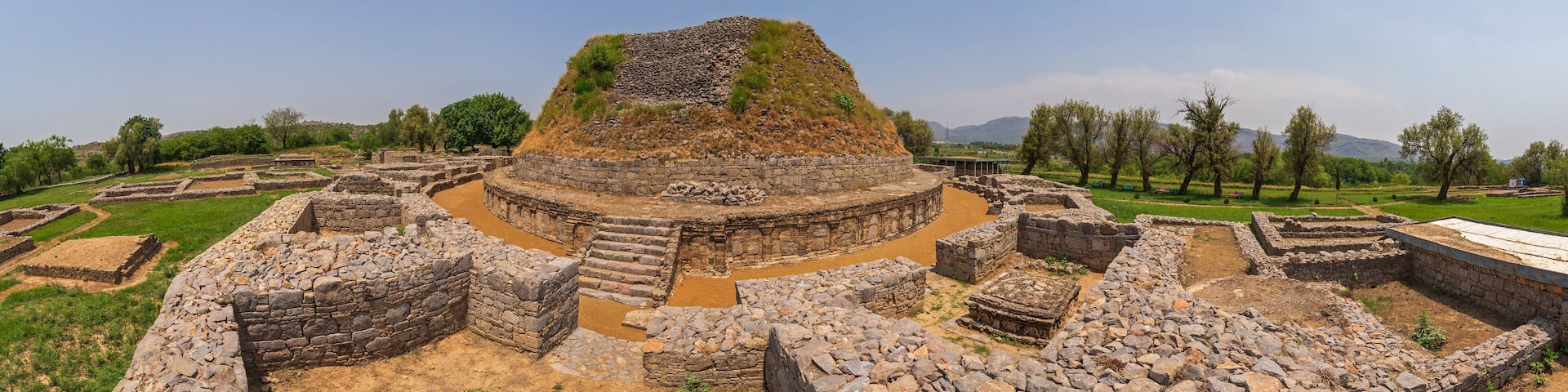 View of the ancient, weathered stone stupa rises majestically under a clear sky amidst the ruins, a testament to history, Taxila, Punjab, Pakistan.