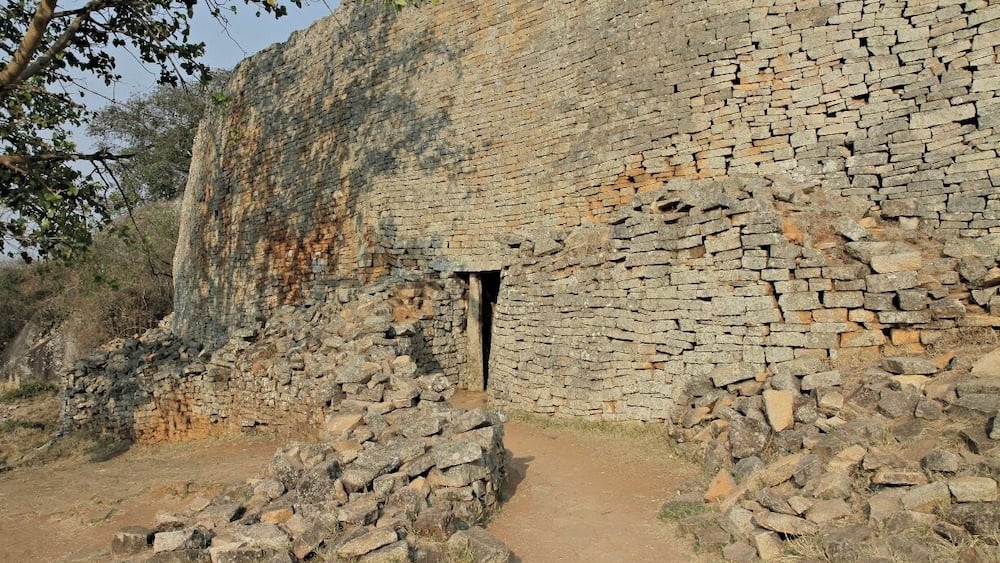 A stone wall with a small doorway, surrounded by scattered rocks and sparse vegetation.