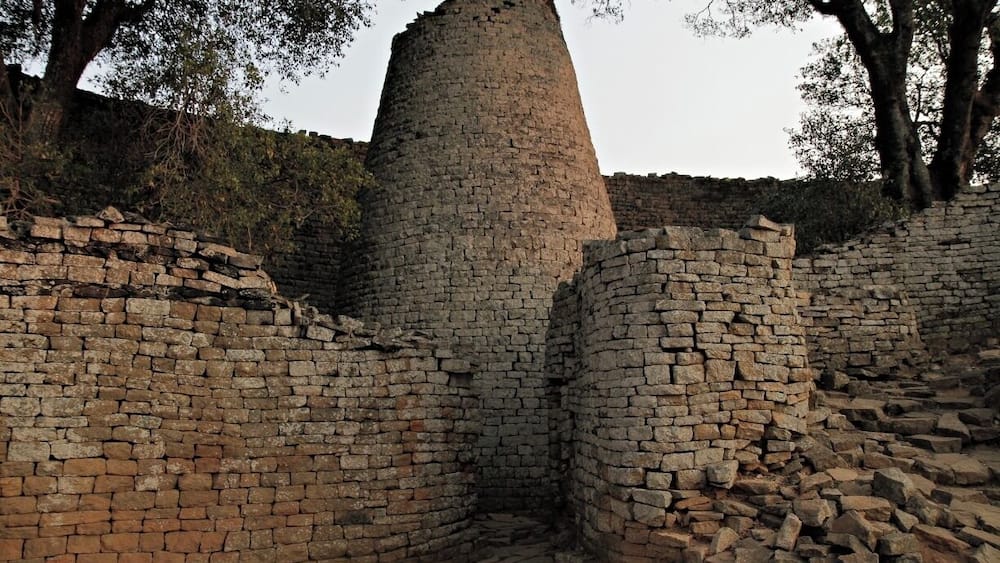 A historical stone structure with a cylindrical tower surrounded by brick walls.