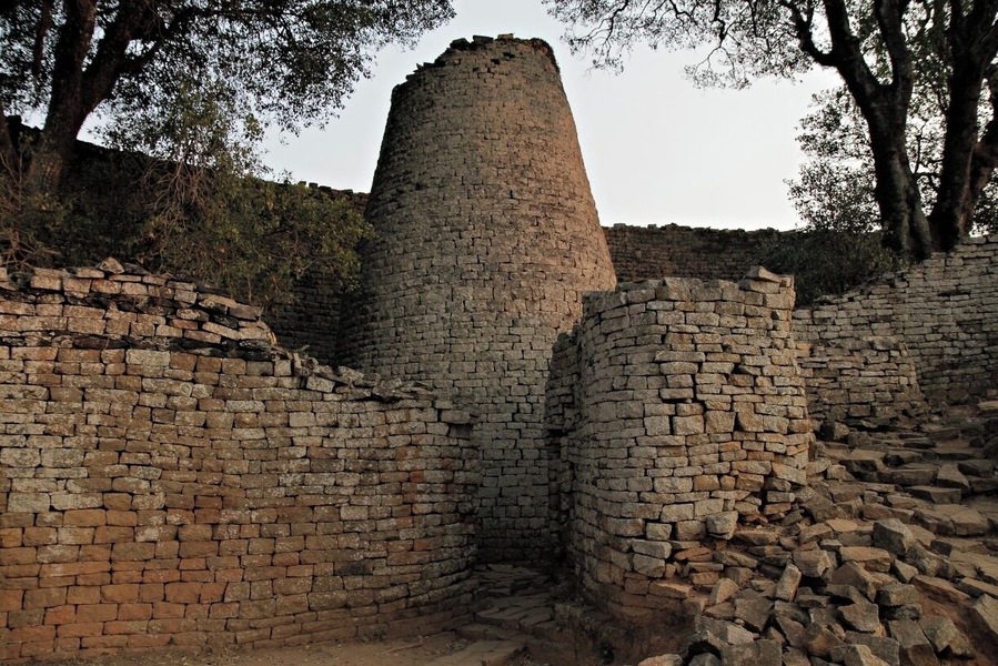 A historical stone structure with a cylindrical tower surrounded by brick walls.