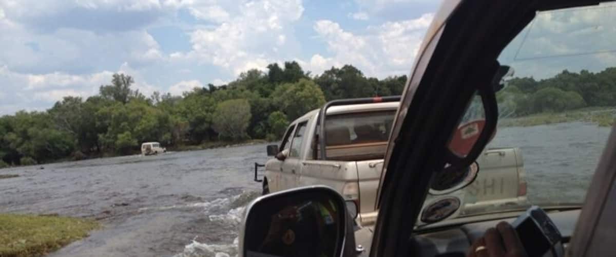 A river with a car driving through it, surrounded by greenery.