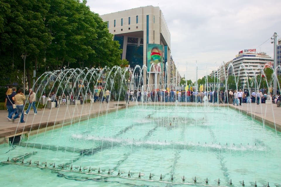 A public square with a large fountain and a modern building with a colorful mural.